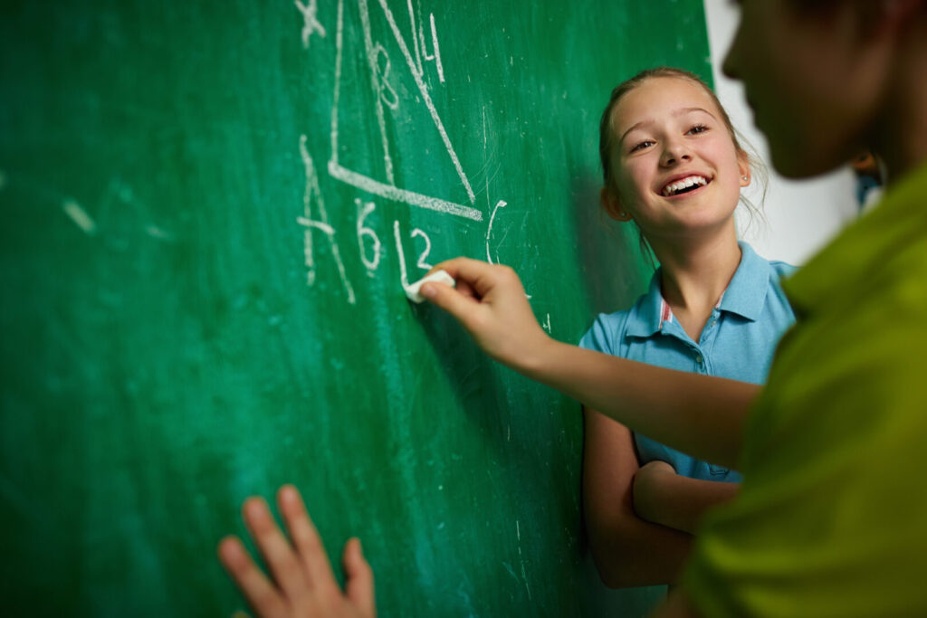 Glad pige ser på sin klassekammerat ved tavlen i matematik